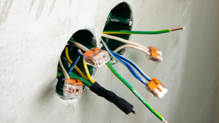 Electrical wiring with connectors emerging from wall openings, illustrating the importance of qualified electricians for safe electrical design services.
