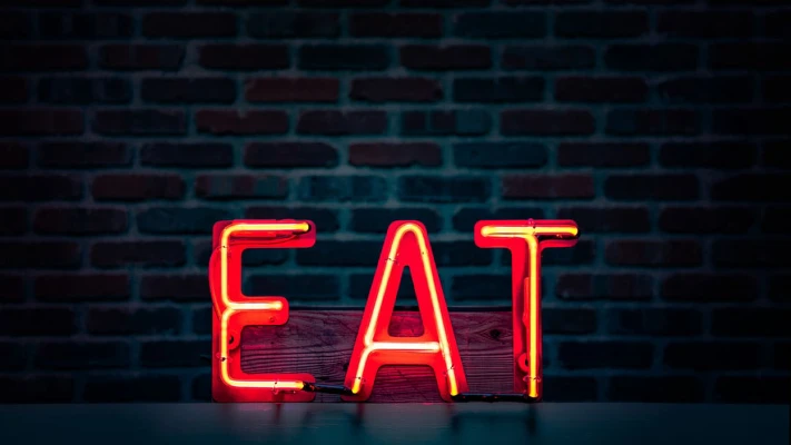 Neon sign spelling "EAT" in bright red against a dark brick wall, emphasizing the importance of restaurant ambiance and electrical services.
