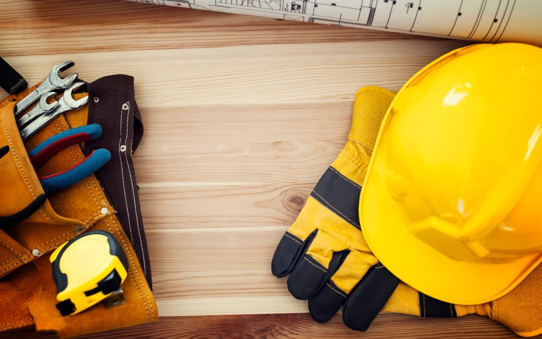 Tools and safety gear including a yellow hard hat, work gloves, and pliers on a wooden surface, symbolizing commercial and industrial electrical services.