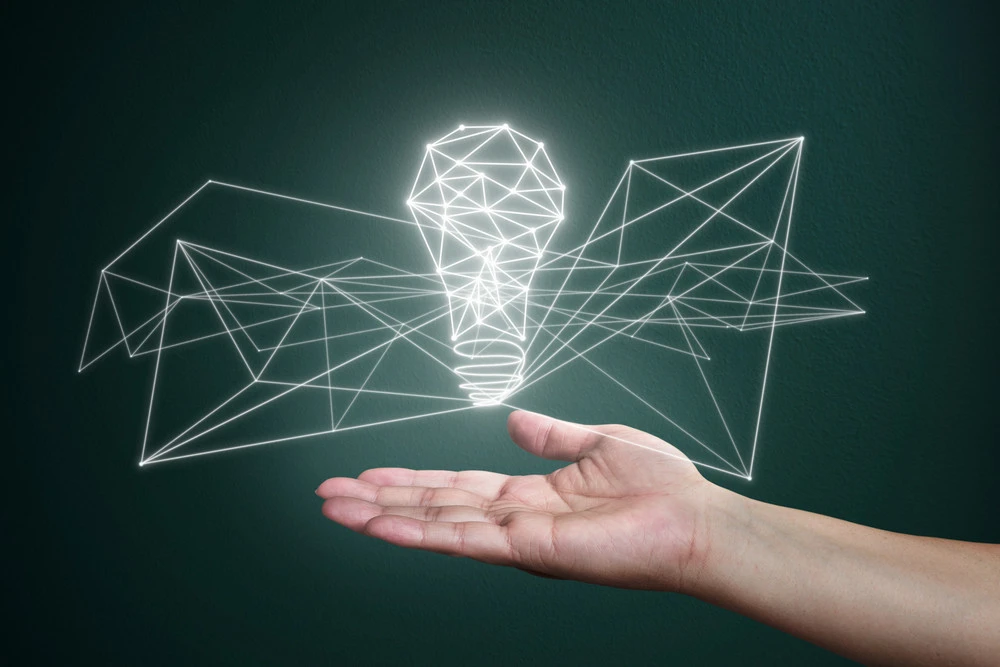Hand holding a glowing wireframe light bulb surrounded by geometric shapes, symbolizing innovative commercial lighting solutions and design concepts.