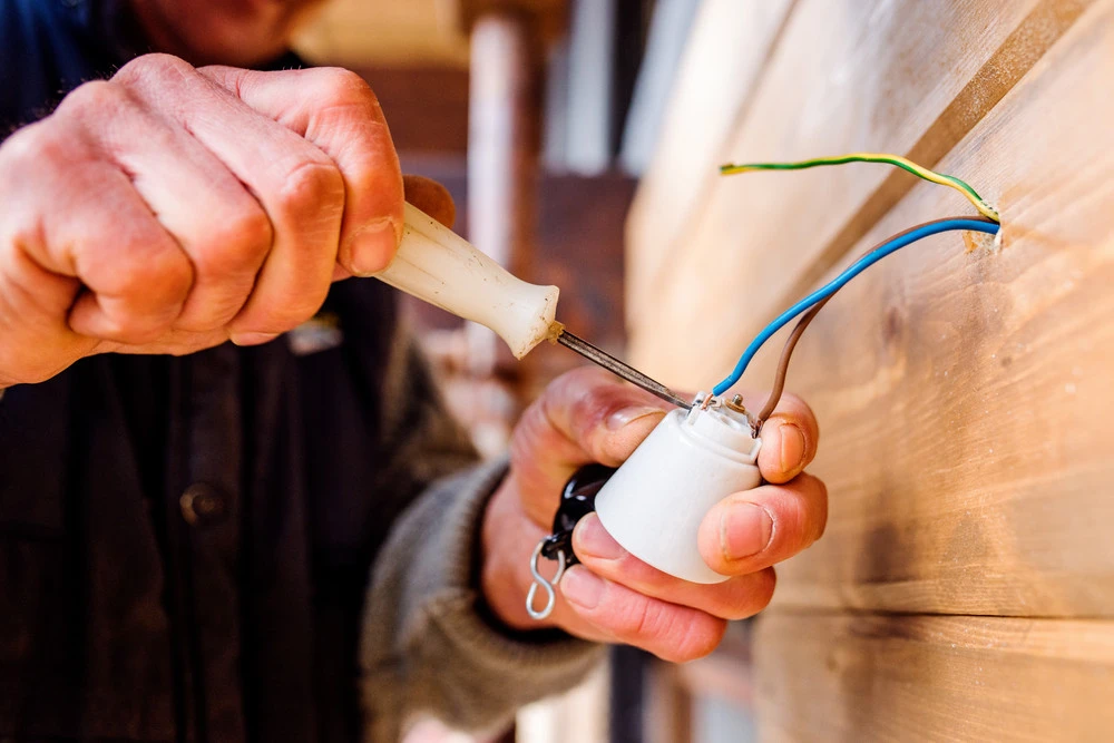 Electrician using a screwdriver to connect wires to a light fixture, demonstrating electrical contracting work relevant to energy efficiency and lowering electric bills.