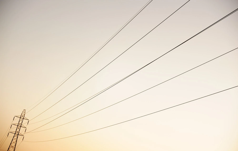 Electric power lines and a transmission tower against a gradient sky, symbolizing residential electrical services and energy-efficient lighting solutions.
