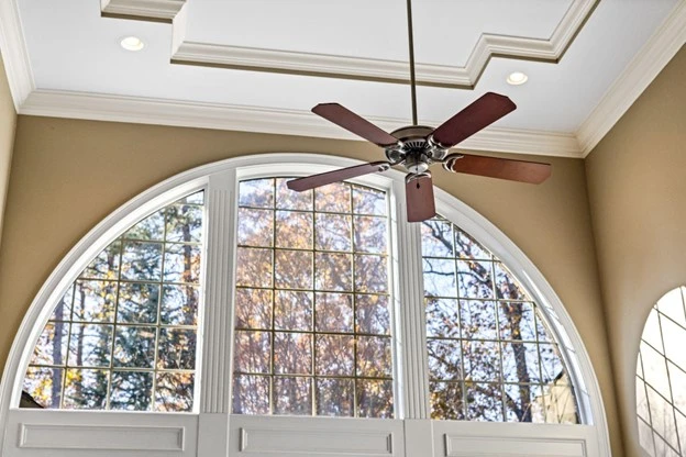 Ceiling fan installed in a spacious room with large arched windows, showcasing proper placement for optimal airflow and aesthetic appeal.