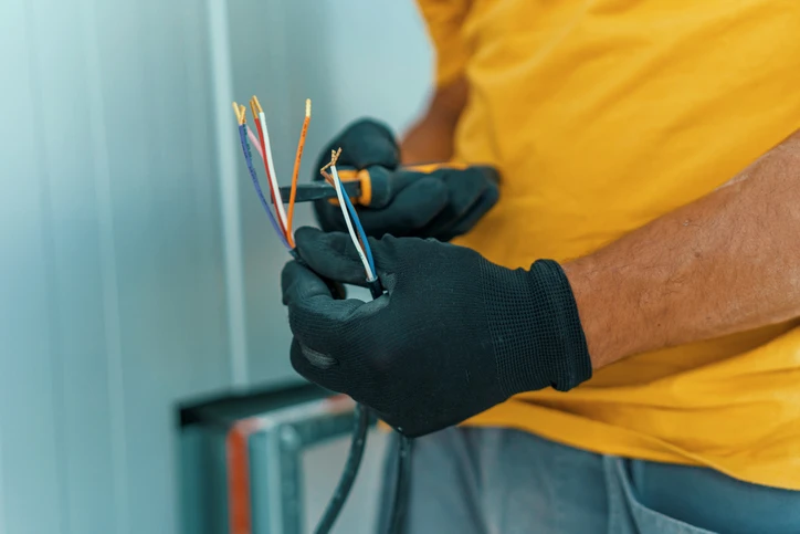 Electrician holding stripped electrical wires, demonstrating safe wiring practices related to preventing electrical shocks in homes.